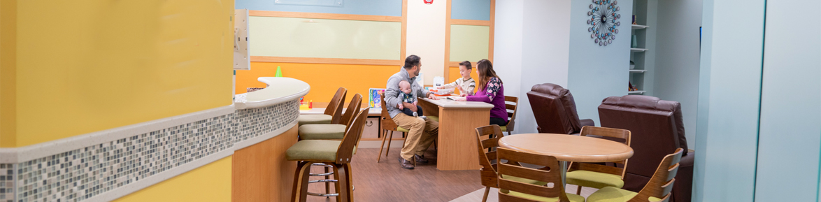 Photo inside Emmett's Place inside Miami Valley Hospital. The room is yellow, blue, green, and orange. A family is sitting at a table coloring with a little boy.